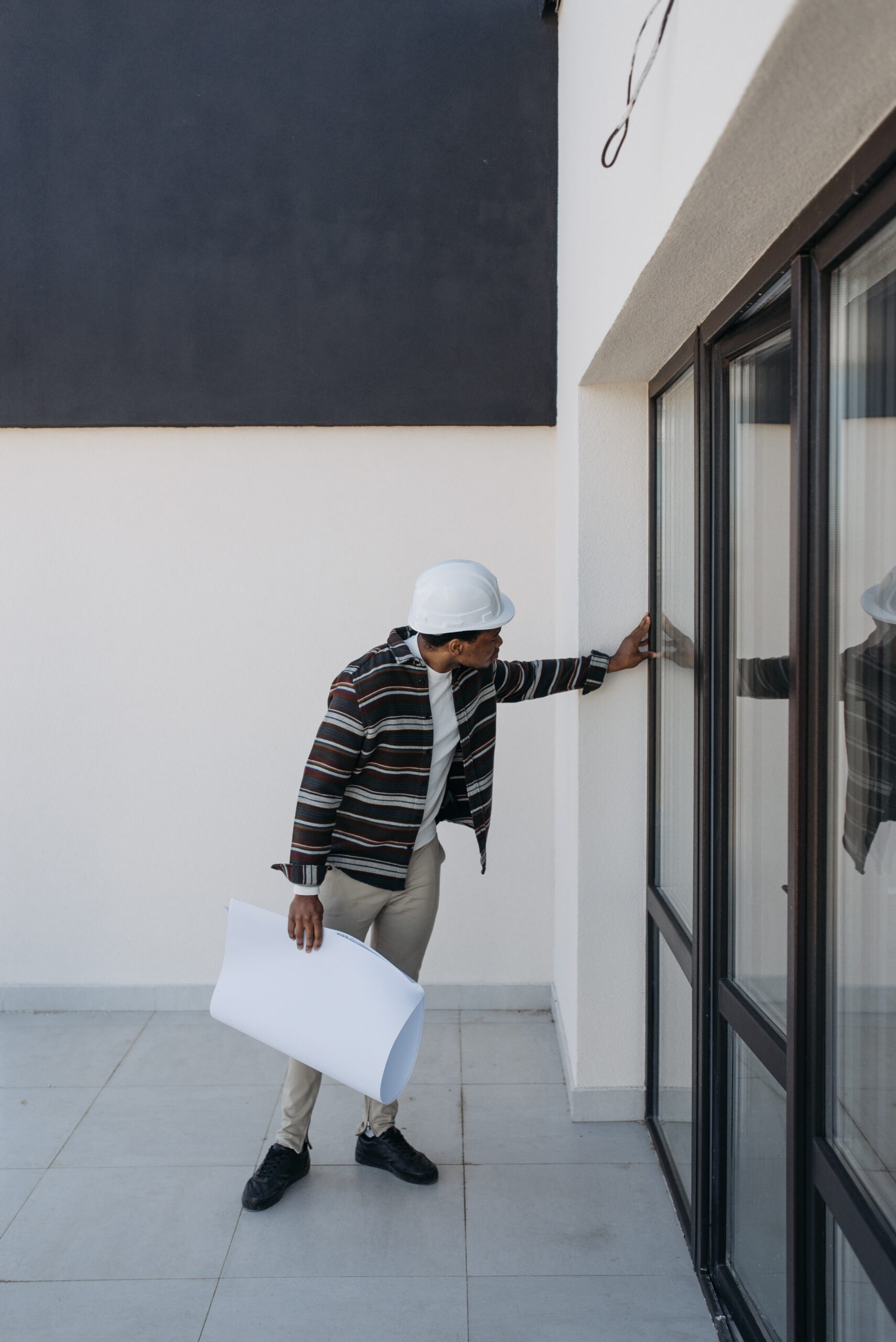 A man in white helmet and striped shirt leaning on the wall.